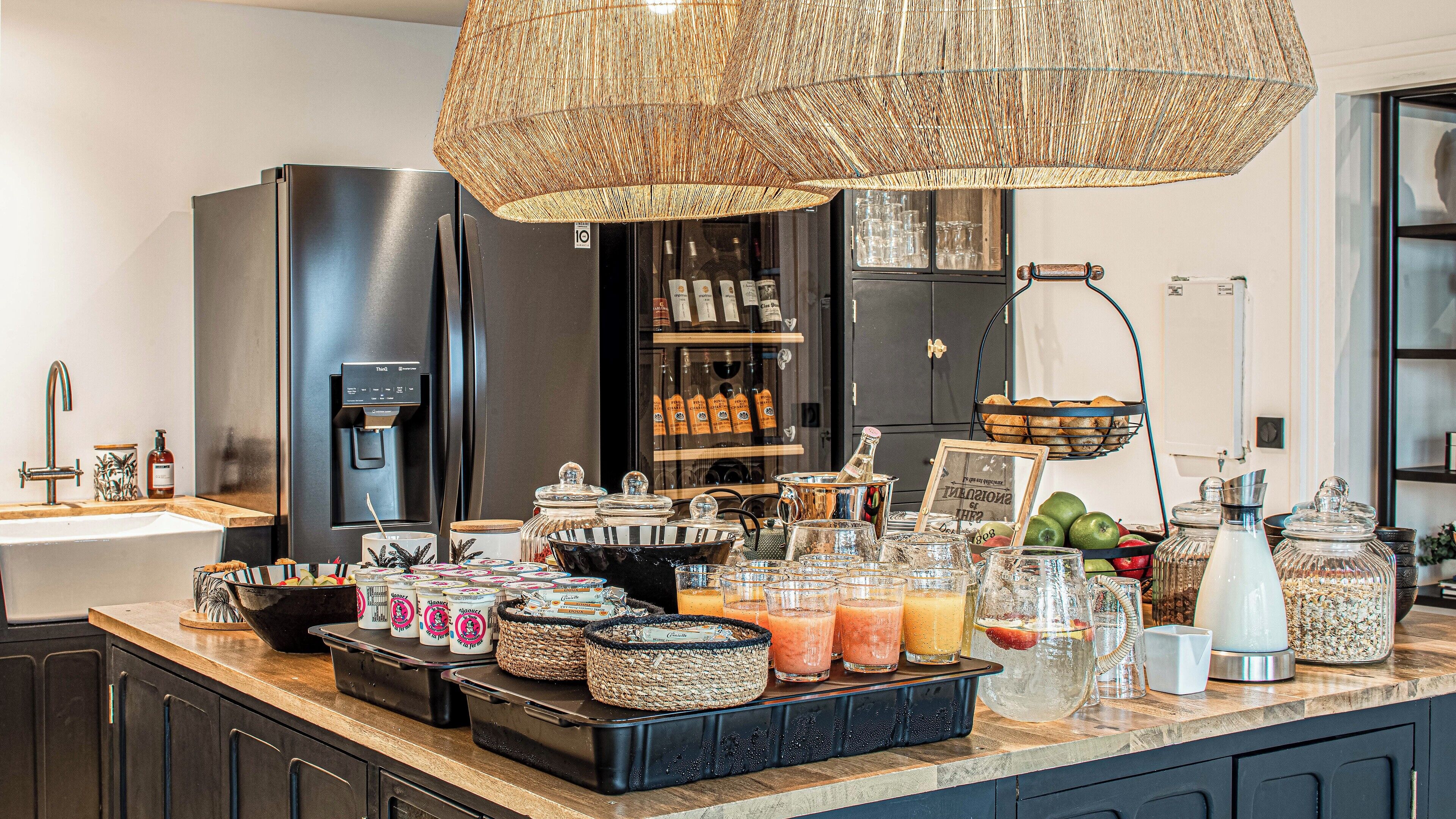 Una cocina con dispensador de agua, un refrigerador y diversos alimentos y bebidas sobre la encimera.