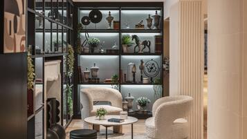 A modern living room with two white armchairs, a round coffee table, and a bookshelf filled with decorative items.