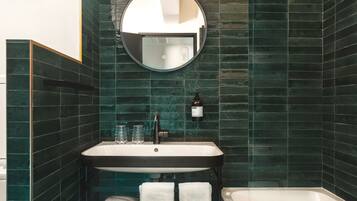 A bathroom with a round mirror, a sink, a bathtub, and two towels.