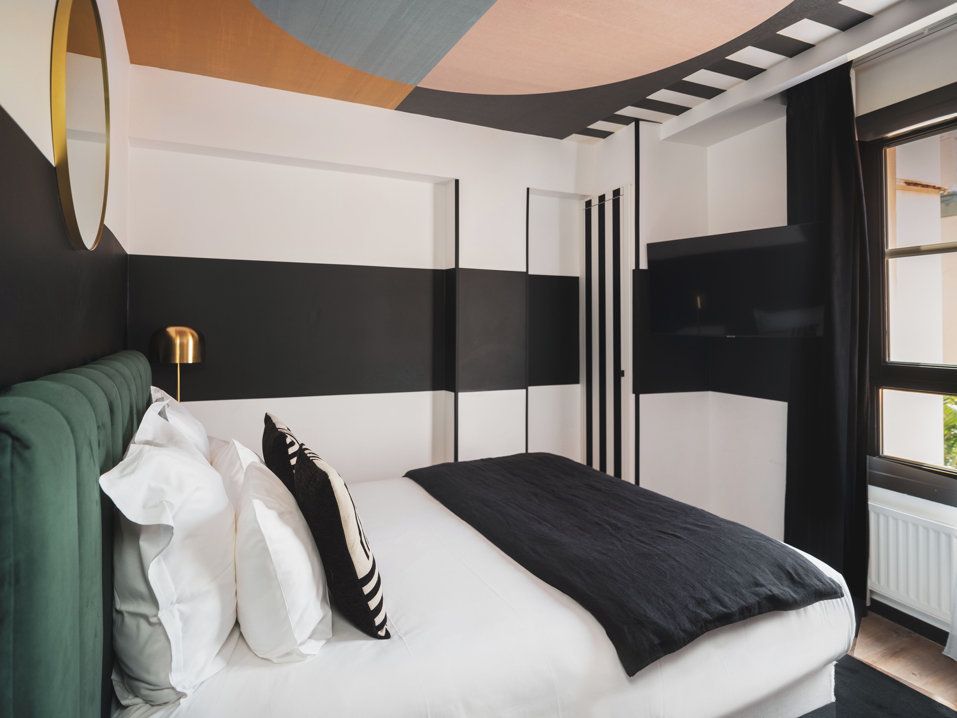 A modern bedroom with a large bed, a green headboard, and a black and white striped wall.