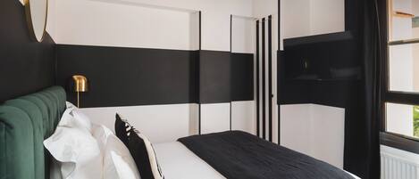 Un dormitorio moderno con una cama grande, cabecera verde y pared a rayas negras y blancas.