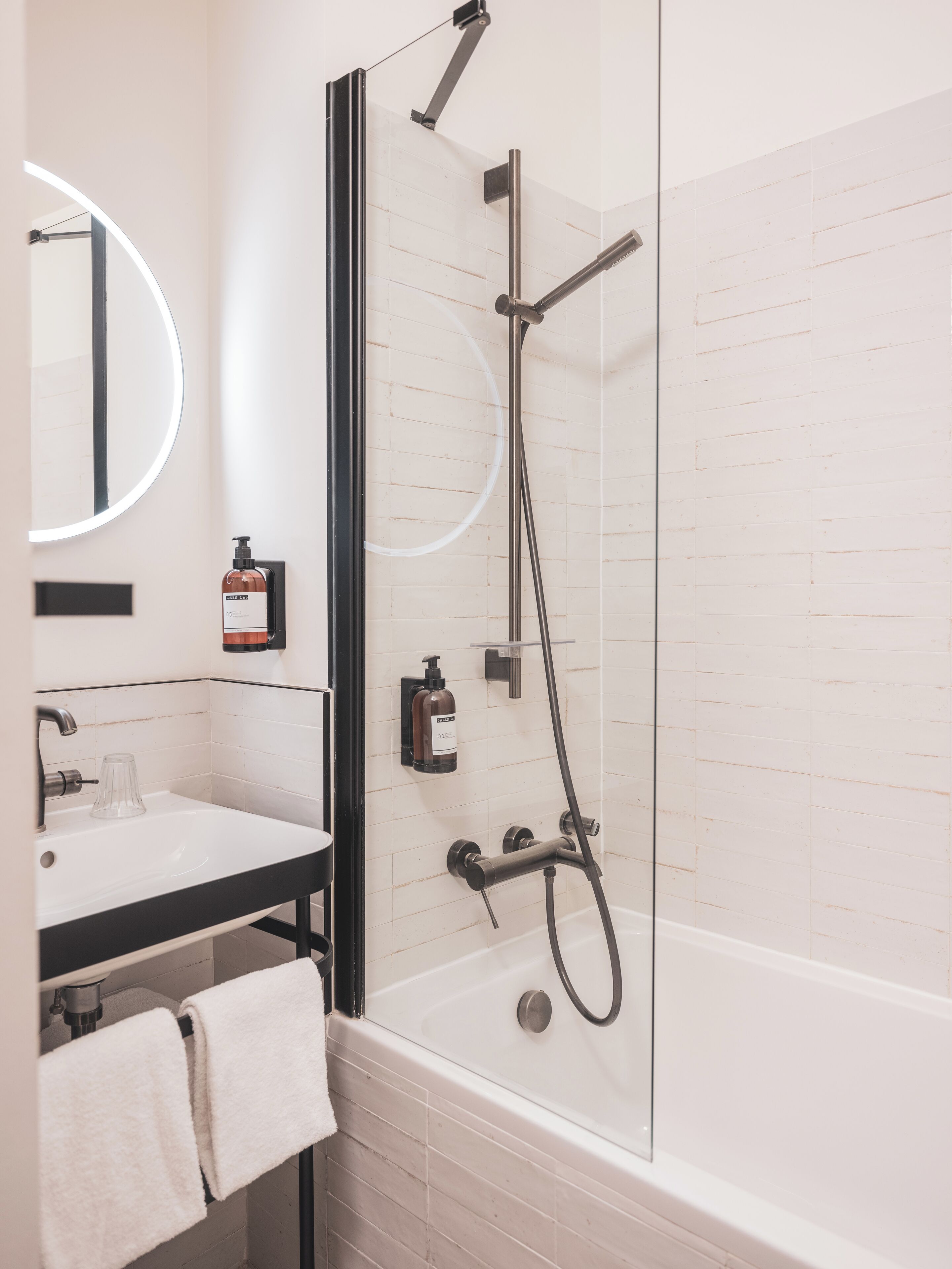 A modern bathroom with a bathtub, a glass-enclosed shower, a sink with a mirror, and a towel rack.