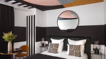 A modern bedroom with a bed, a round mirror, a side table, a chair, and a vase with plants.