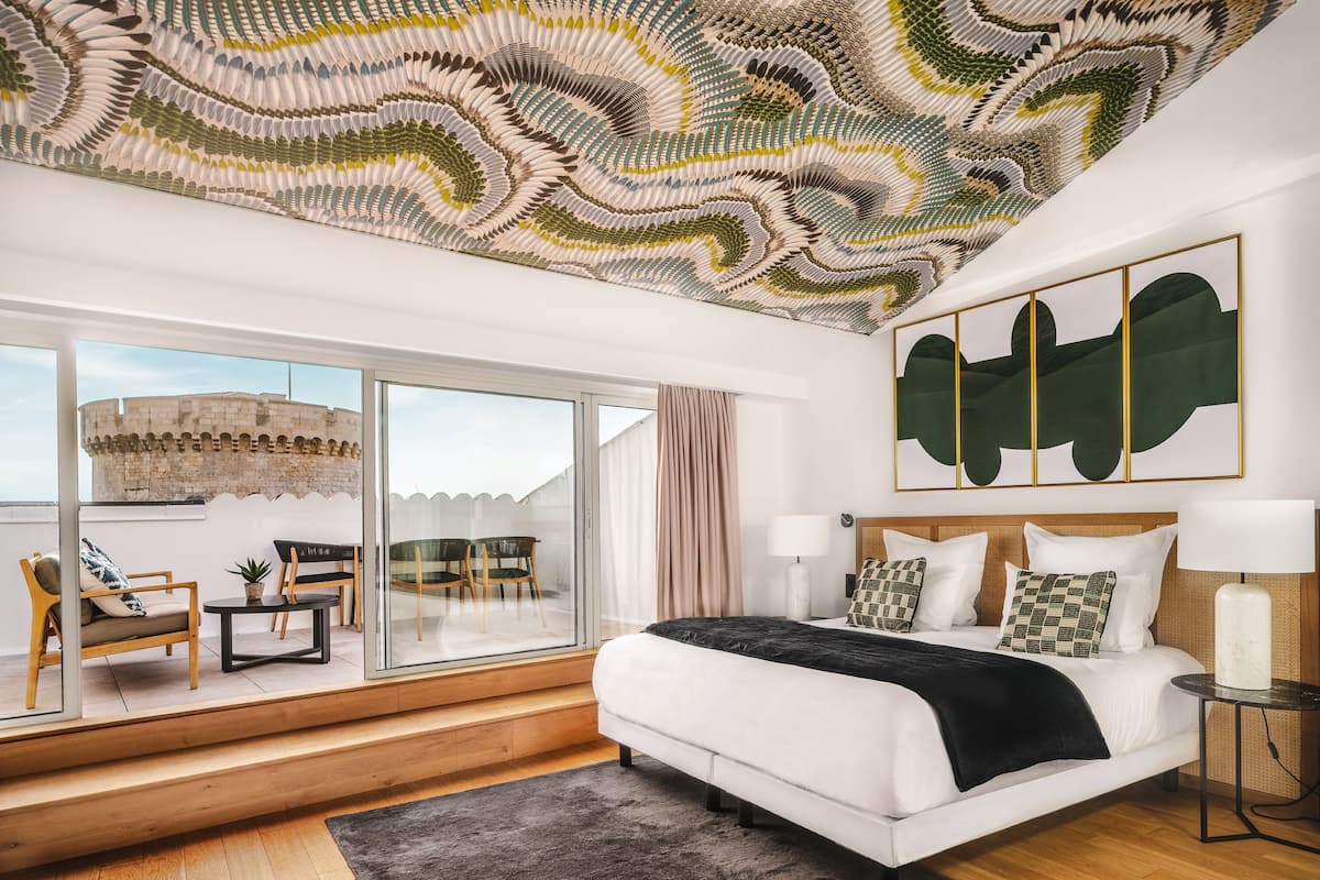 Un dormitorio moderno con una cama grande, vistas de un castillo a través de ventanas de piso a techo y un diseño de techo único.