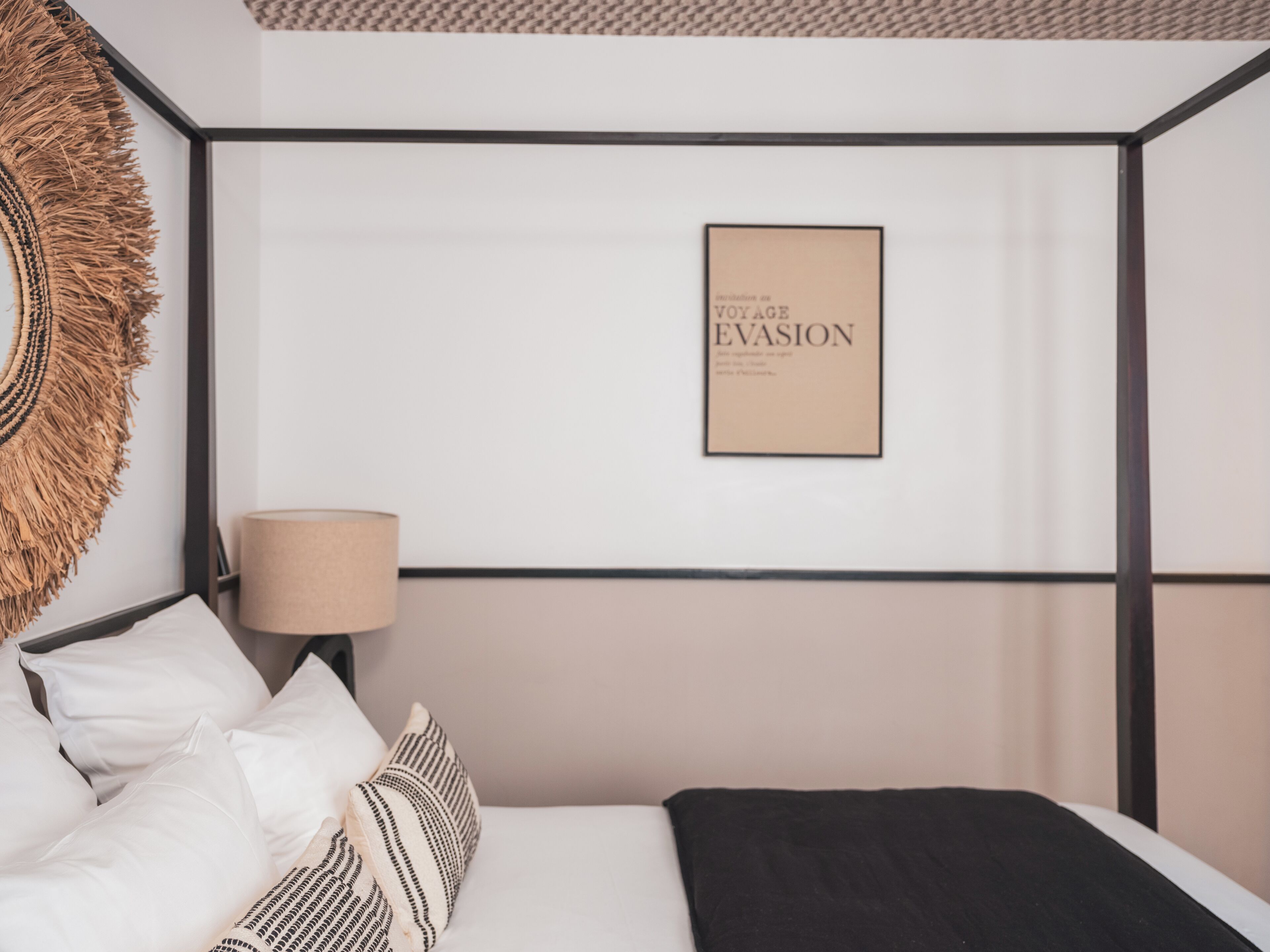 Quarto bem arrumado com cama, travesseiros, um porta-retrato na parede e uma luminária.