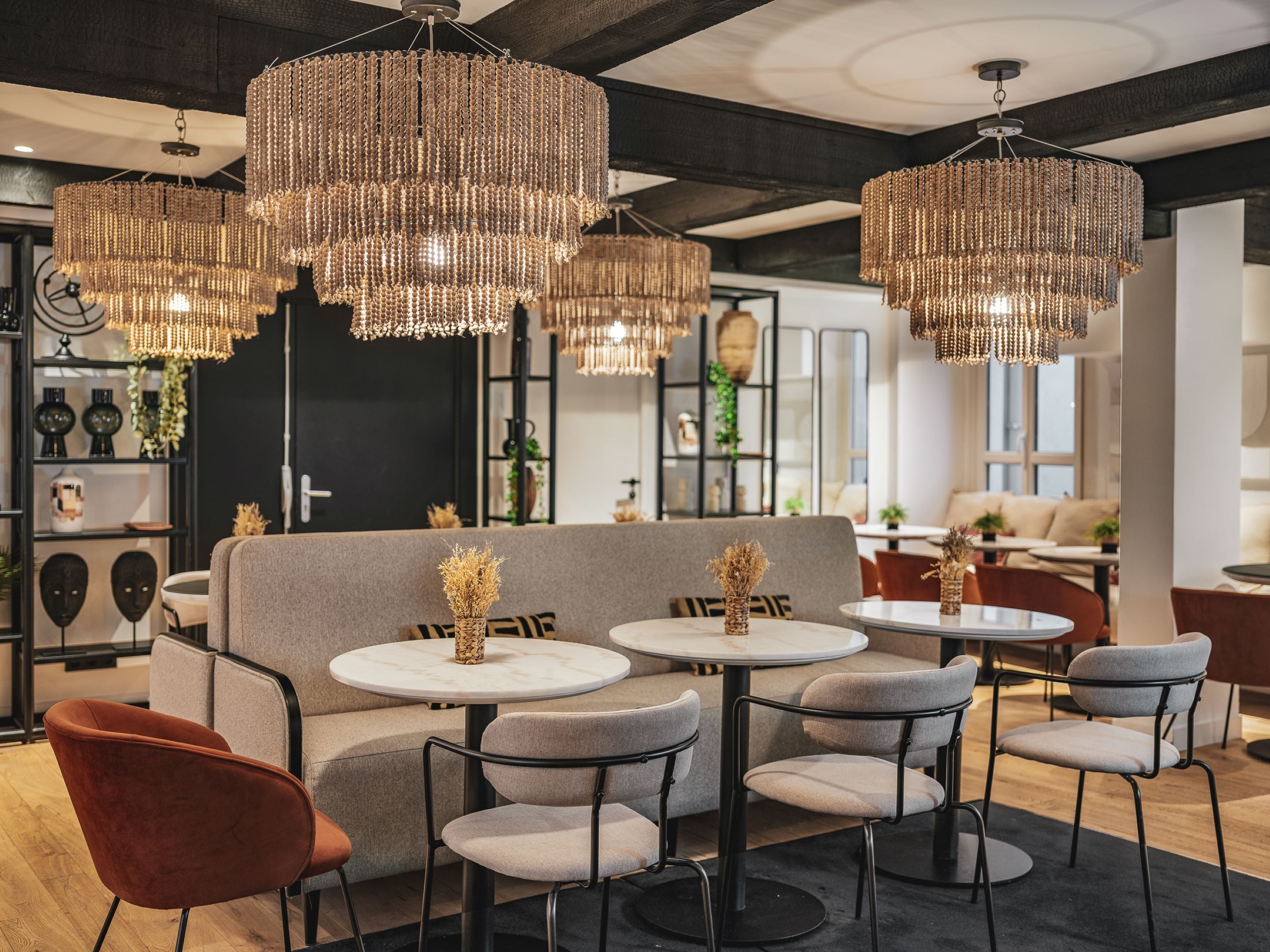 A modern interior with a grey sofa, round tables, and chairs, and decorative beaded chandeliers.