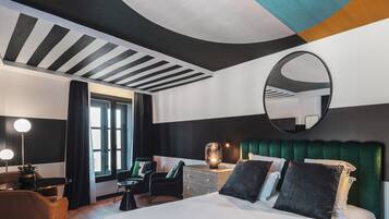 Una habitación de hotel moderna con una cama grande, un espejo redondo, un cabecero tapizado de verde y una pequeña mesa con una lámpara.