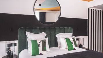 Una habitación de hotel moderna con una cama grande, cabecera tapizada en verde y un espejo redondo encima.