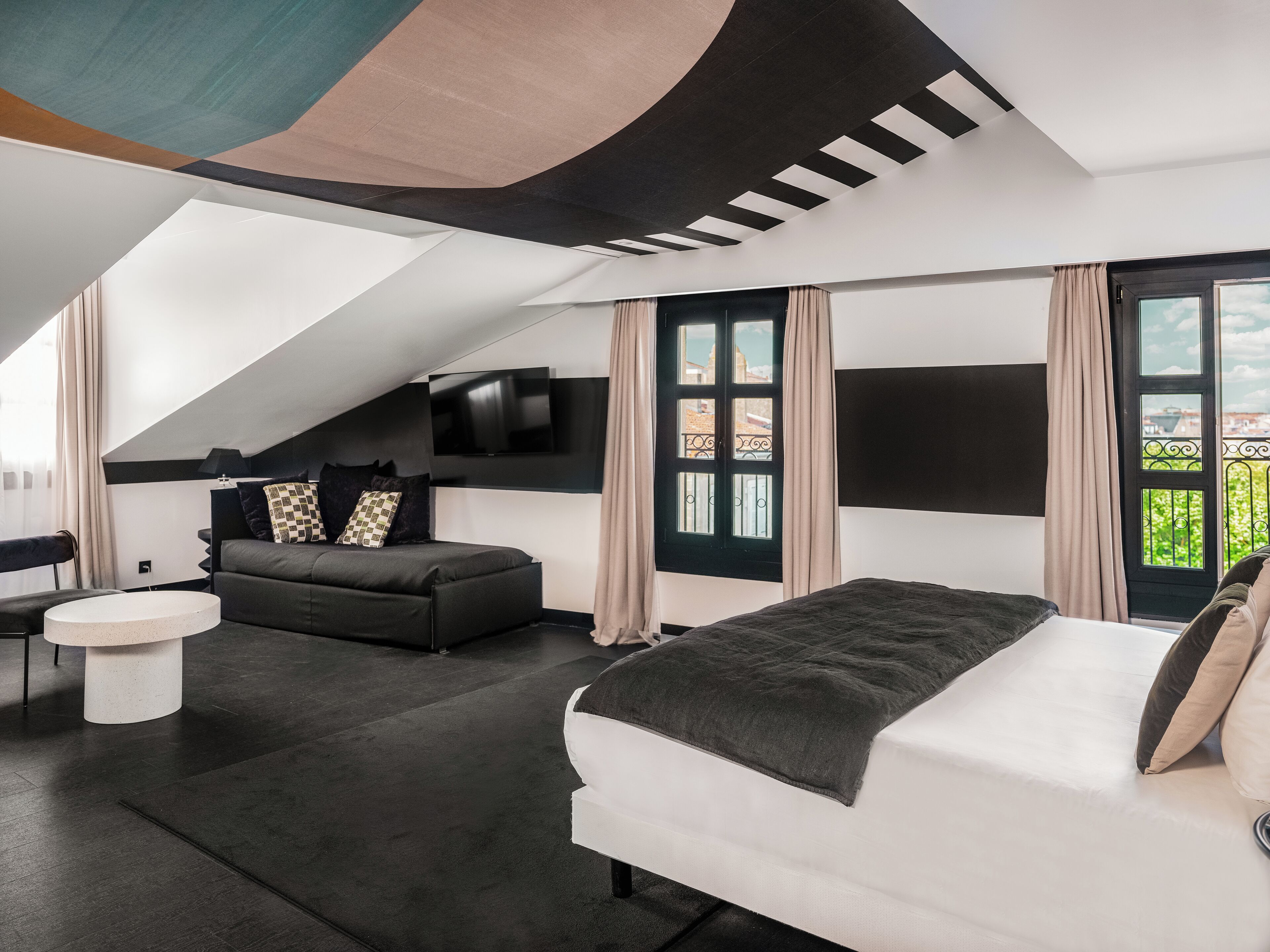 Un dormitorio moderno con una cama grande, un sofá, un televisor y vistas al balcón.