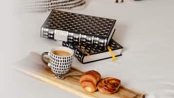 Ein ordentlich angerichtetes Frühstück mit einer Kaffeetasse, Gebäck und Büchern auf einem Tablett.