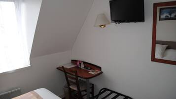 A small, well-lit room with a bed, a desk with a chair, a television, and a window with curtains.
