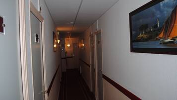 A hotel hallway with doors on the left, a framed painting on the right, and a carpeted floor.