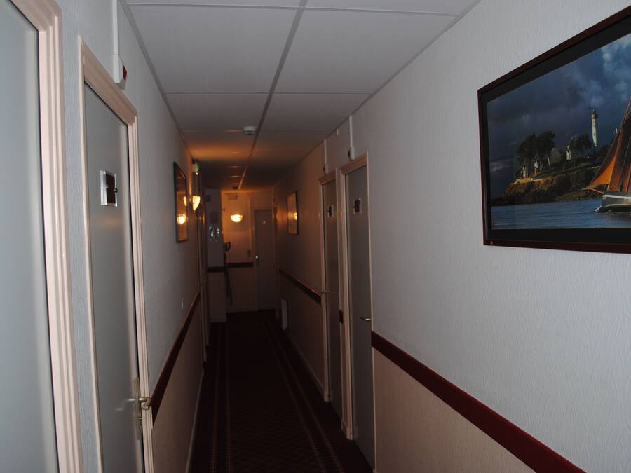 A hotel hallway with doors on the left, a framed painting on the right, and a carpeted floor.