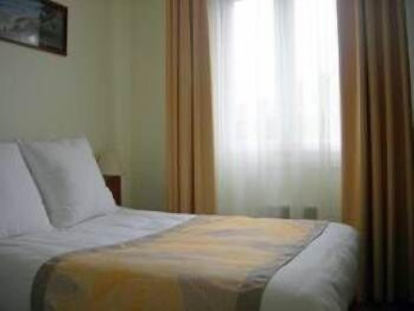 Una habitación de hotel con cama, mesita de noche y ventana con cortinas.
