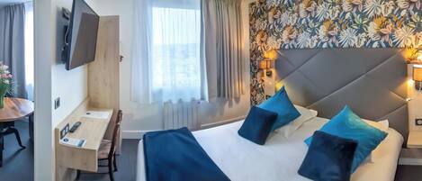 Habitación de hotel con cama, lámparas de noche, un escritorio con silla, televisor montado en la pared y ventana con cortinas.