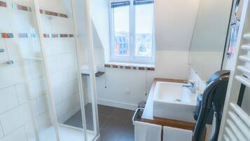 A modern bathroom with a glass shower enclosure, a window with a view, a sink with a mirror, and a towel rack.