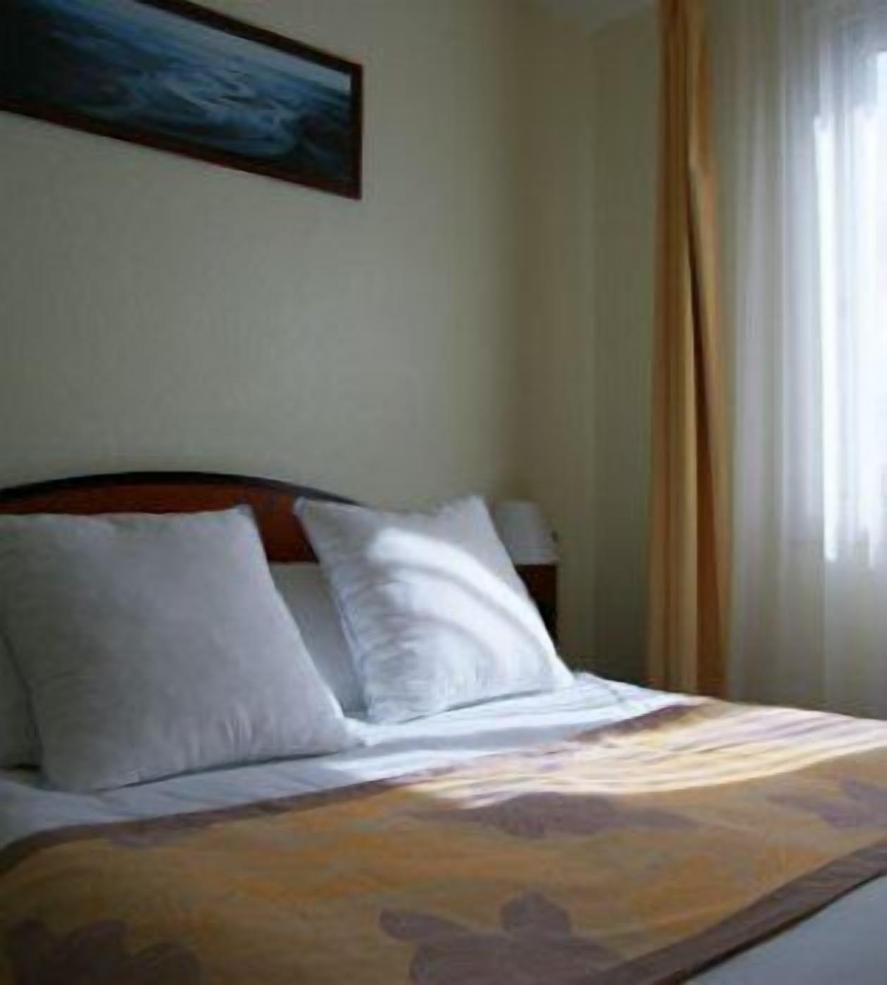 A hotel room with a bed, pillows, a nightstand, and a painting on the wall.