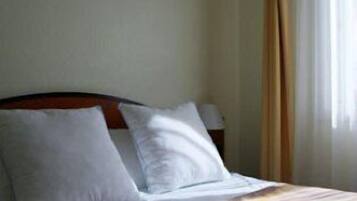 A hotel room with a bed, pillows, a nightstand, and a painting on the wall.