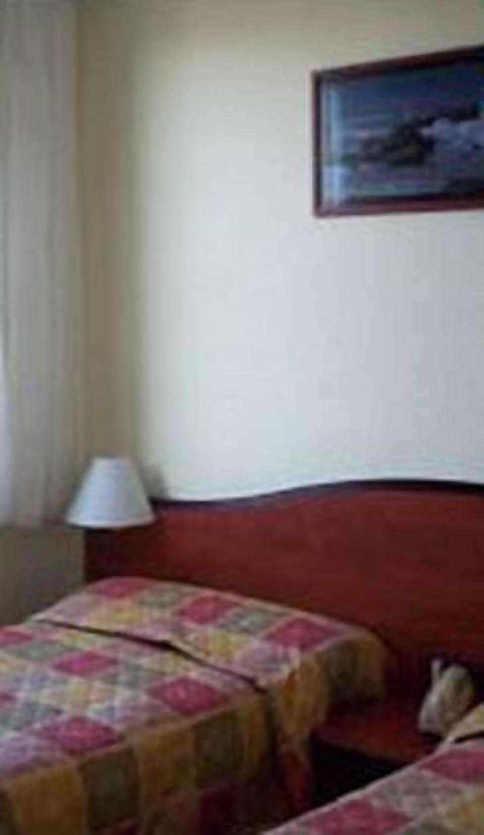 A hotel room with two beds, a nightstand, a lamp, and a framed picture on the wall.