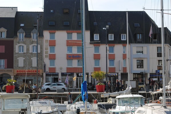 Un puerto deportivo con barcos amarrados, un edificio con un letrero que dice "BOULANGERIE" y un asta con una bandera.