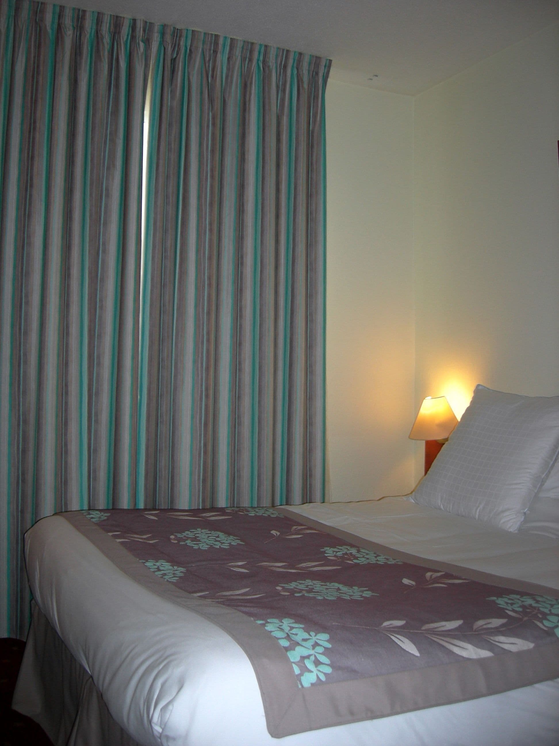 A hotel room with a bed, a lamp, and curtains.