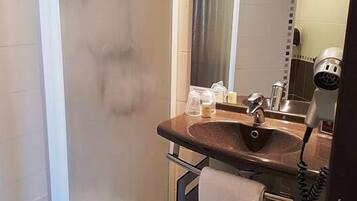 A modern bathroom with a glass shower enclosure, a sink with a towel, and a hairdryer.