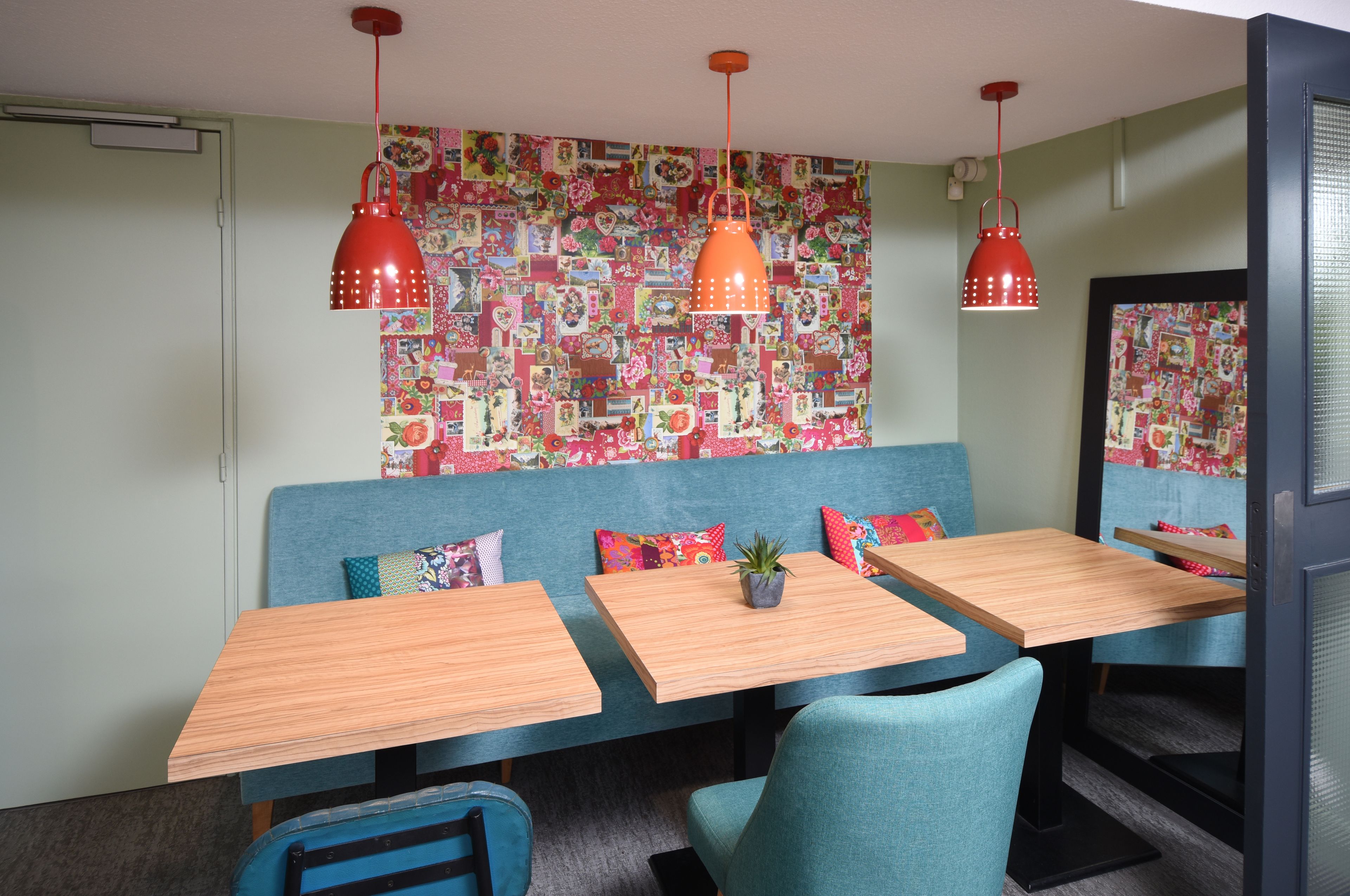 Un espace repas avec des banquettes bleues, des tables en bois et des lampes suspendues rouges.