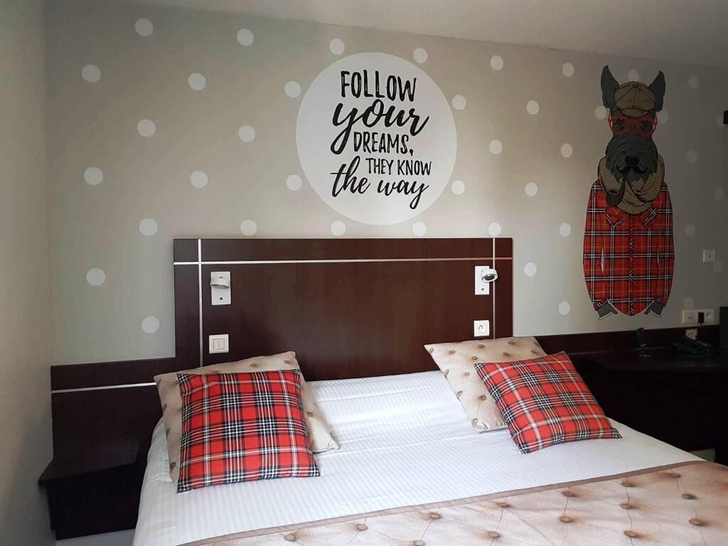 A hotel room with a bed, two pillows, a headboard, and a wall decoration.