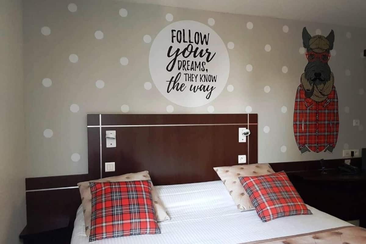 A hotel room with a bed, two pillows, a headboard, and a wall decoration.