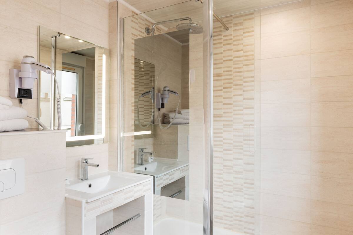 Un baño moderno con ducha envuelta en vidrio, un lavabo blanco y un espejo grande.