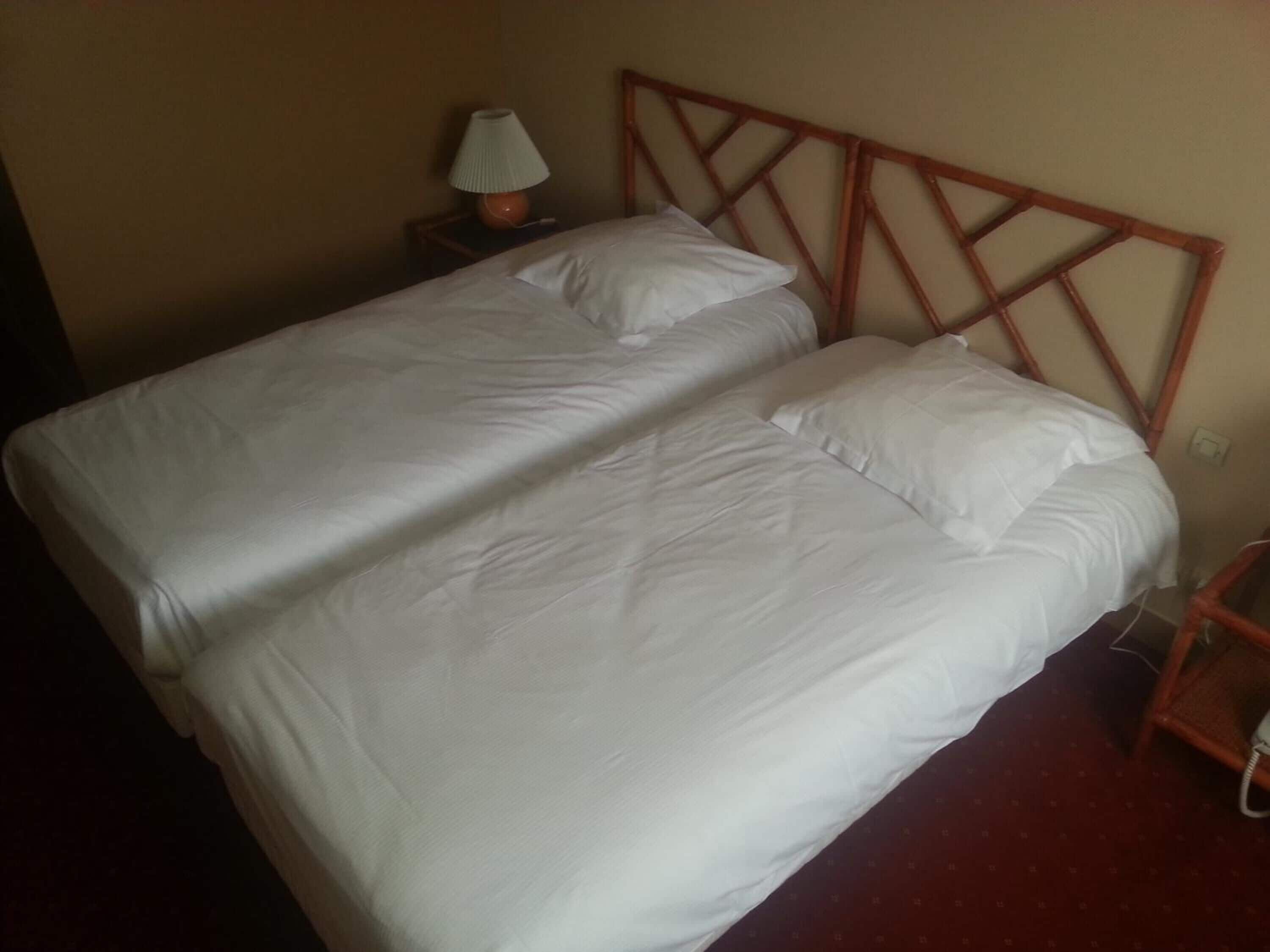 Ein Einzelbett mit hölzernem Kopfteil, ein Nachttisch mit Lampe und ein Telefon.