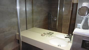 A modern bathroom with a glass shower enclosure, a double sink vanity, and a handheld mirror.