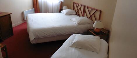 A hotel room with two single beds, a wooden headboard, a nightstand with a lamp, and a radiator.