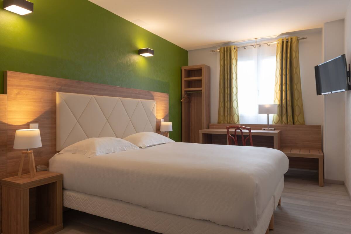 Una habitación de hotel con una cama grande, lámparas de noche, un escritorio, una silla, un televisor y un armario.