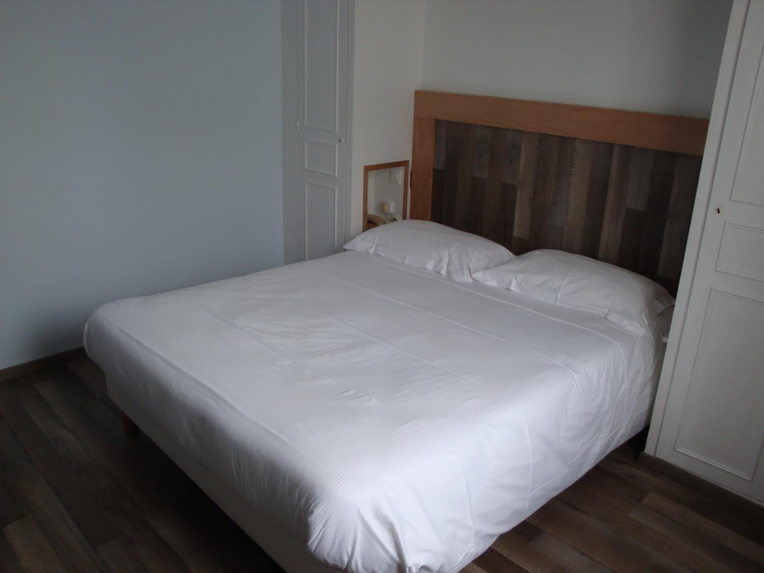 Habitación individual con una cama de madera, ropa de cama blanca y piso de madera.