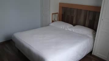 A single-bed room with a wooden headboard, white bedding, and a wooden floor.