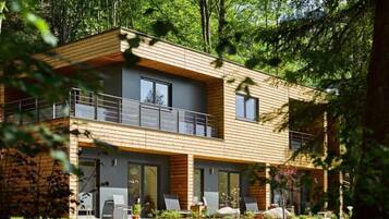 A modern two-story house with a wooden exterior, large windows, and a balcony.