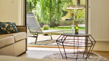 A room with a sofa, a table with a bottle, and a view of greenery outside.