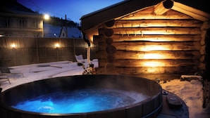 Una cabaña de madera con un jacuzzi en la nieve.