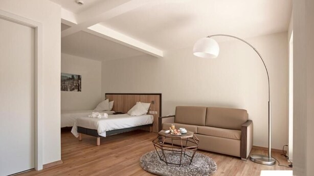 A modern bedroom with a bed, a sofa, a coffee table, and a floor lamp. - Hotel De La Poste - Logis De France (Le Bonhomme)