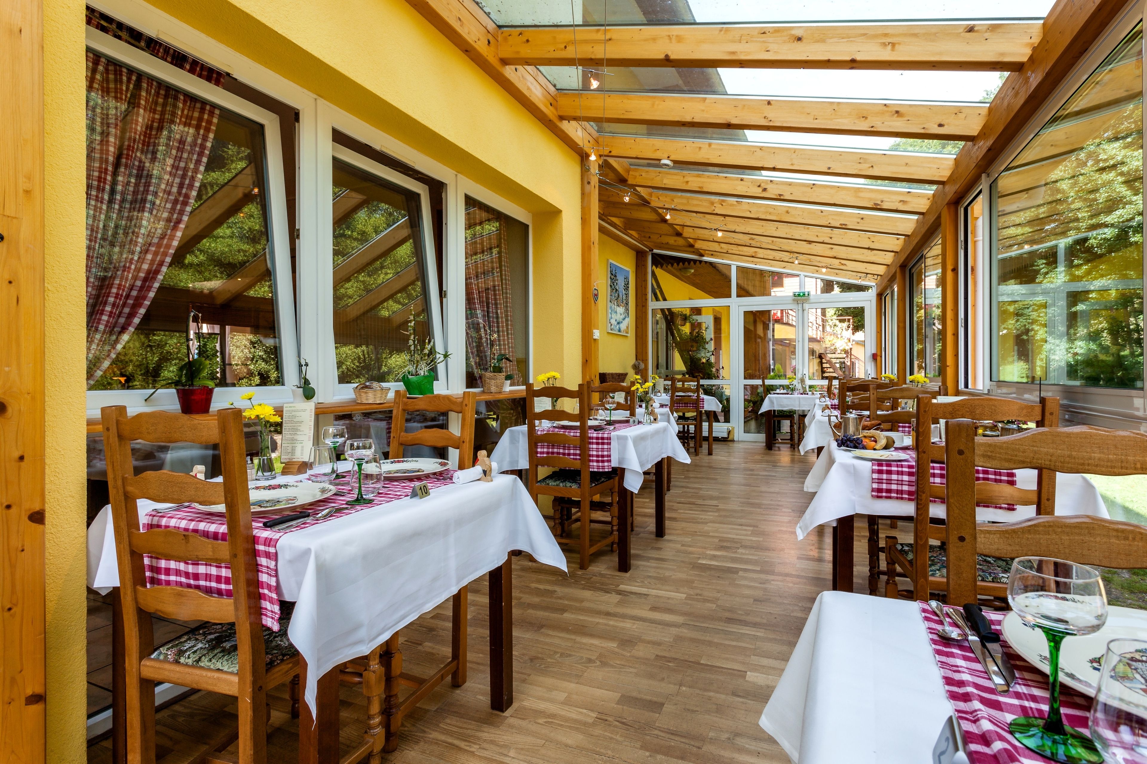 A restaurant with wooden tables and chairs, covered dining area, and large windows.