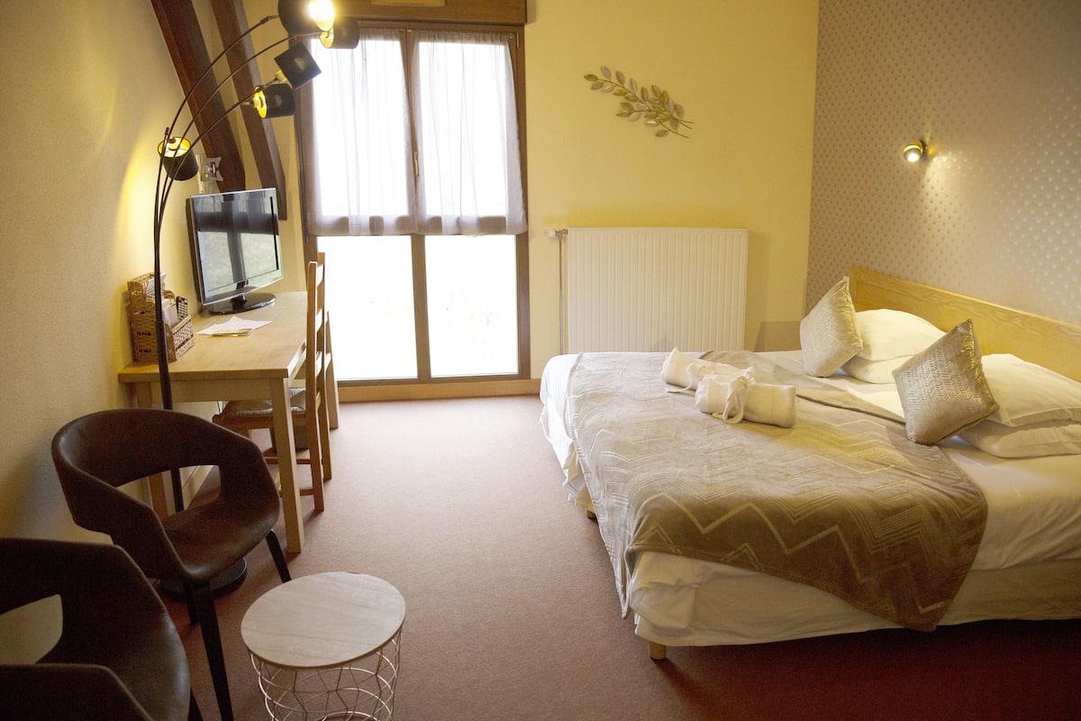 A hotel room with a bed, a desk with a computer, two chairs, and a small round table.