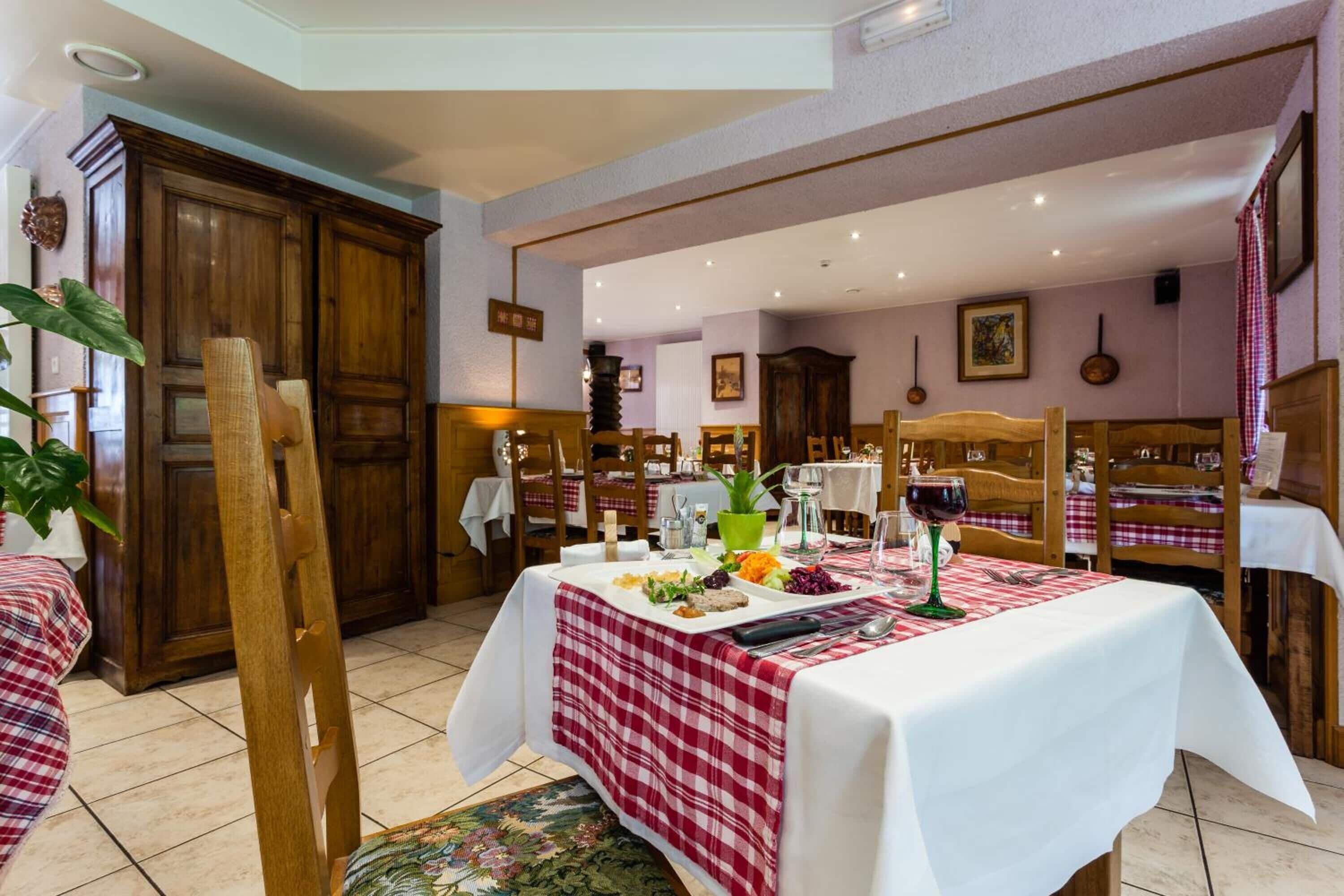 Un área de comedor con una mesa dispuesta para dos personas, con mantel a cuadros rojos y blancos, una botella de vino tinto y diferentes platos.