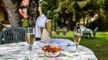 A round table with a floral tablecloth, two wine glasses, a bottle of champagne, and a bowl of nuts.