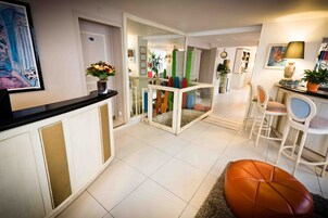 A modern interior with a reception desk, a glass partition, and a seating area with chairs and a cushioned bench.