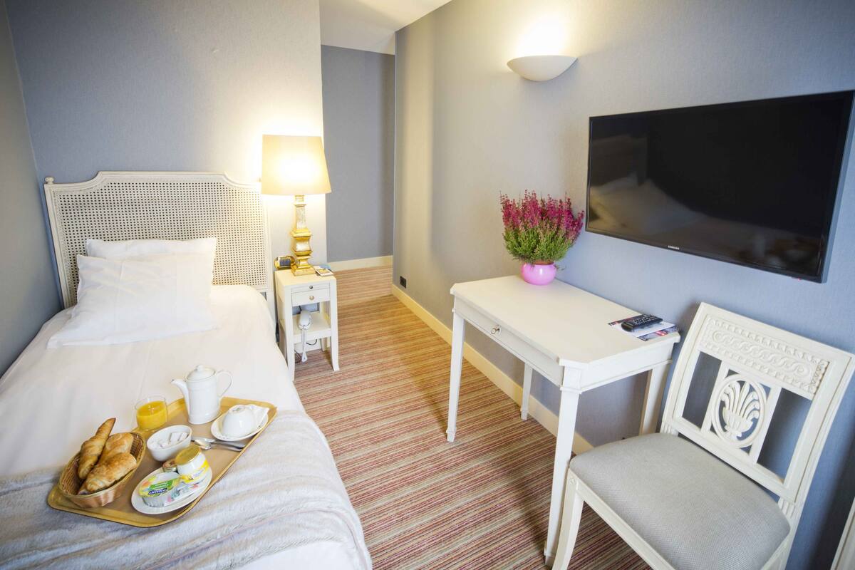 Hotellihuone, jossa on sänky, yöpöytä, tuoli, televisio ja aamiaistarjoilu.