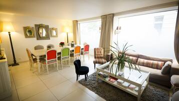 A living room with a dining area, a sofa, a coffee table, and a large window with curtains.