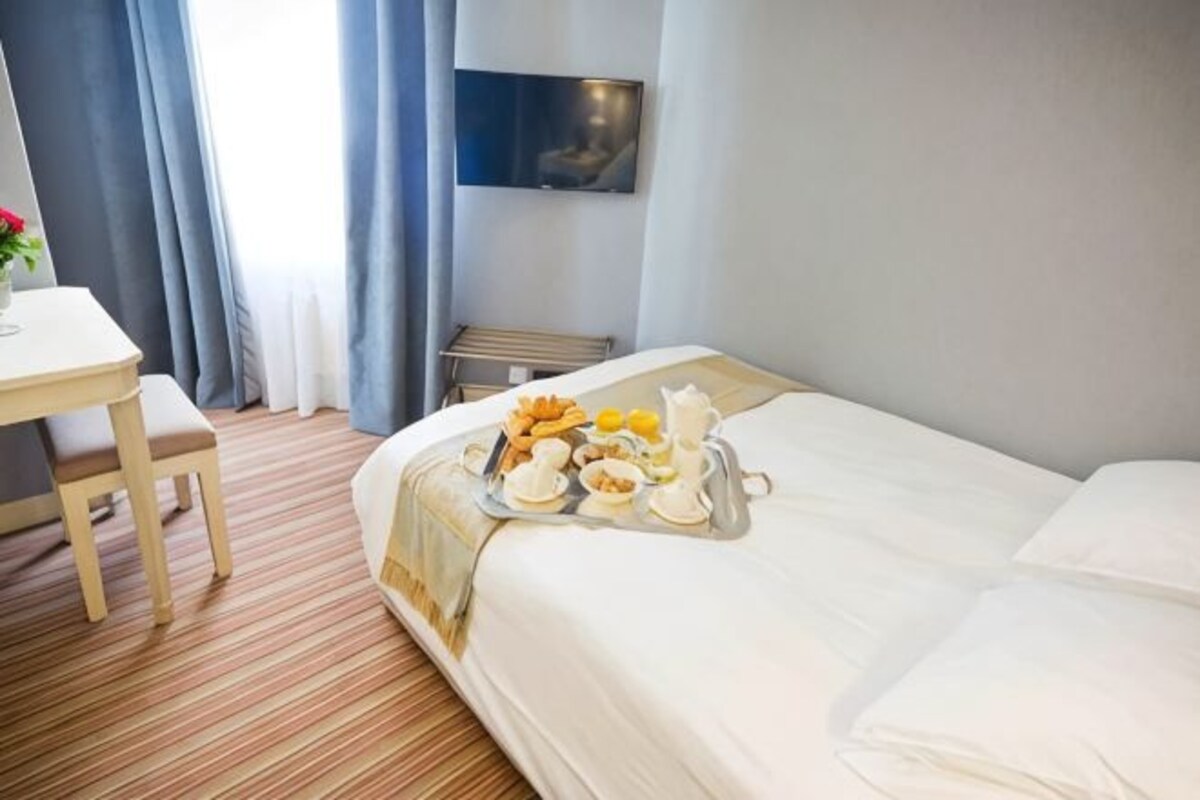 A hotel room with a bed, a dining table, and a tray of breakfast items.