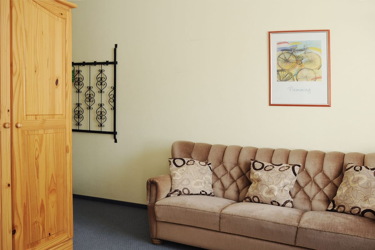 Ein Zimmer mit einem Holzschrank, einem beigen Sofa mit gemusterten Kissen und einem gerahmten Kunstwerk an der Wand.
