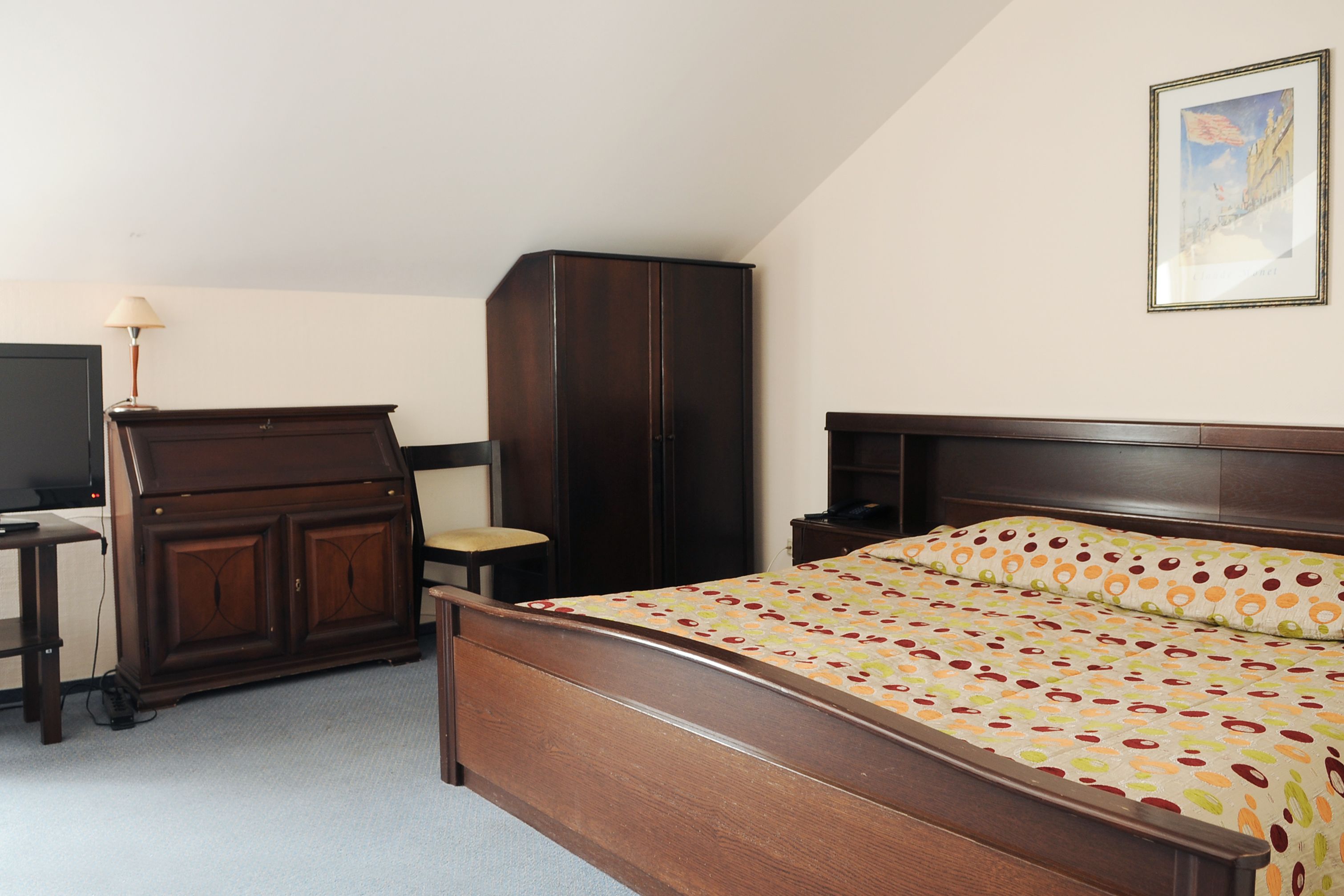 Un dormitorio con cama de madera, un armario, un escritorio con lámpara y una silla.